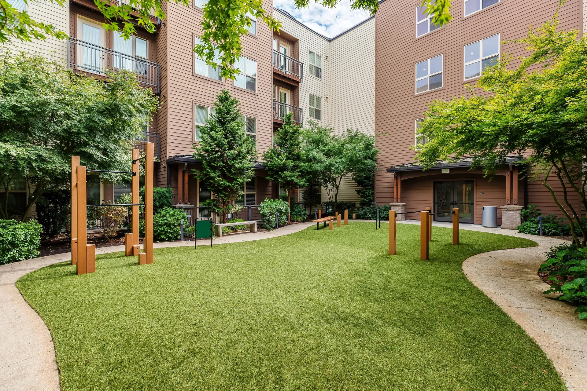Outdoor apartment courtyard with green lawn, trees, benches, and exercise posts at Tessera at Orenco Station.