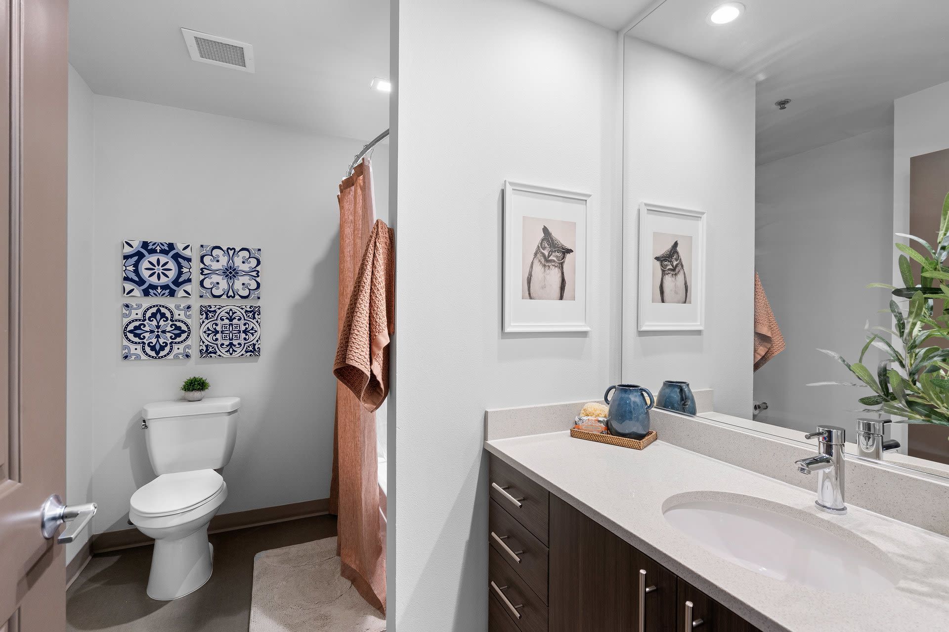 Apartment bathroom with a single vanity, sink, mirror, toilet, and pink shower curtain at Tessera at Orenco Station.