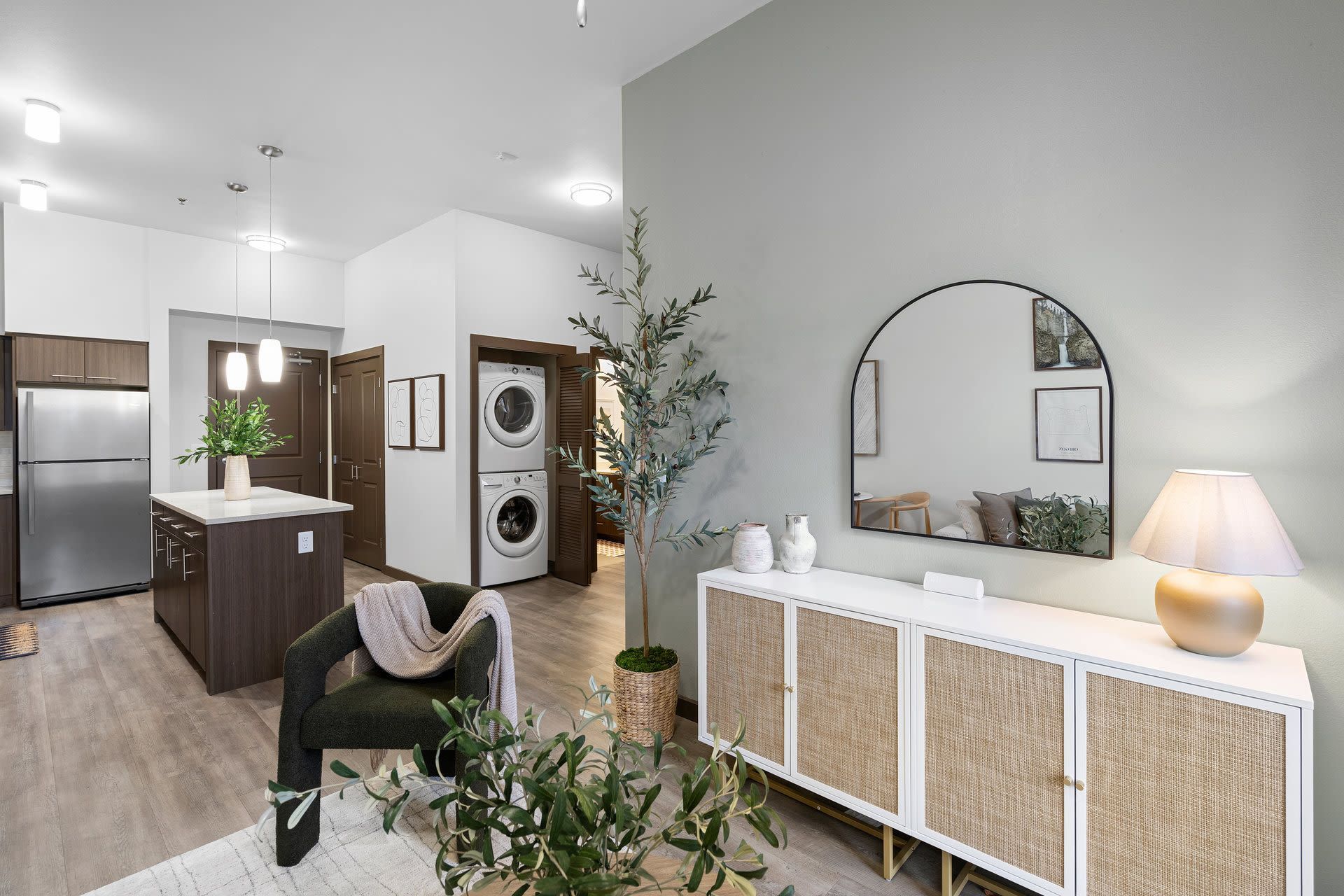 Open-concept living space with kitchen island, stainless steel fridge, and stacked laundry near a doorway at Tessera at Orenco Station at Tessera at Orenco Station.