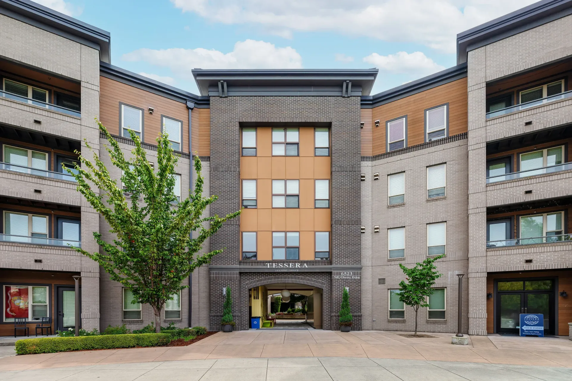 Modern apartment building exterior with central archway entrance and landscaped courtyard at Tessera at Orenco Station.