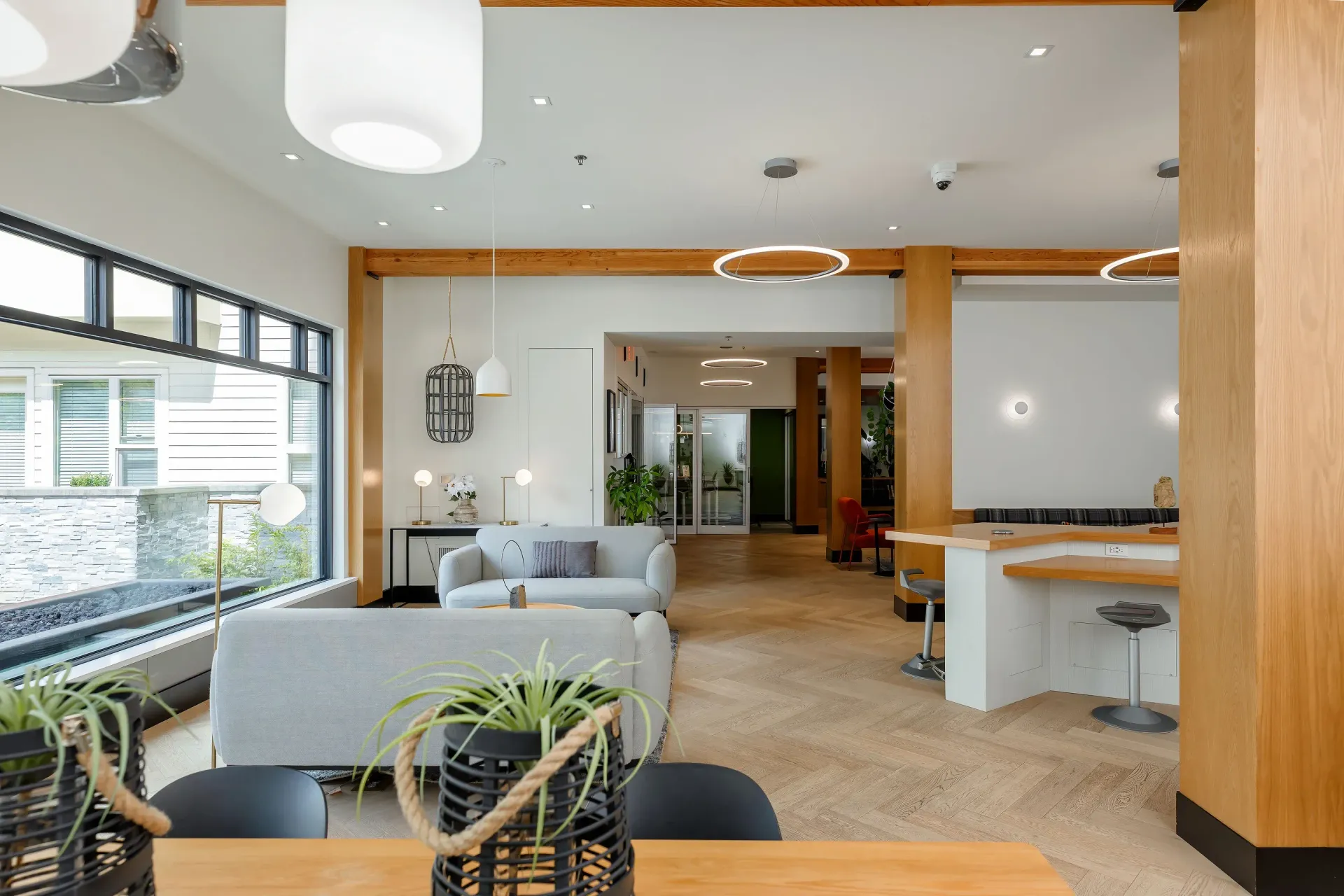 Bright modern community lounge with beige sofas, plants, and large windows at Tessera at Orenco Station.