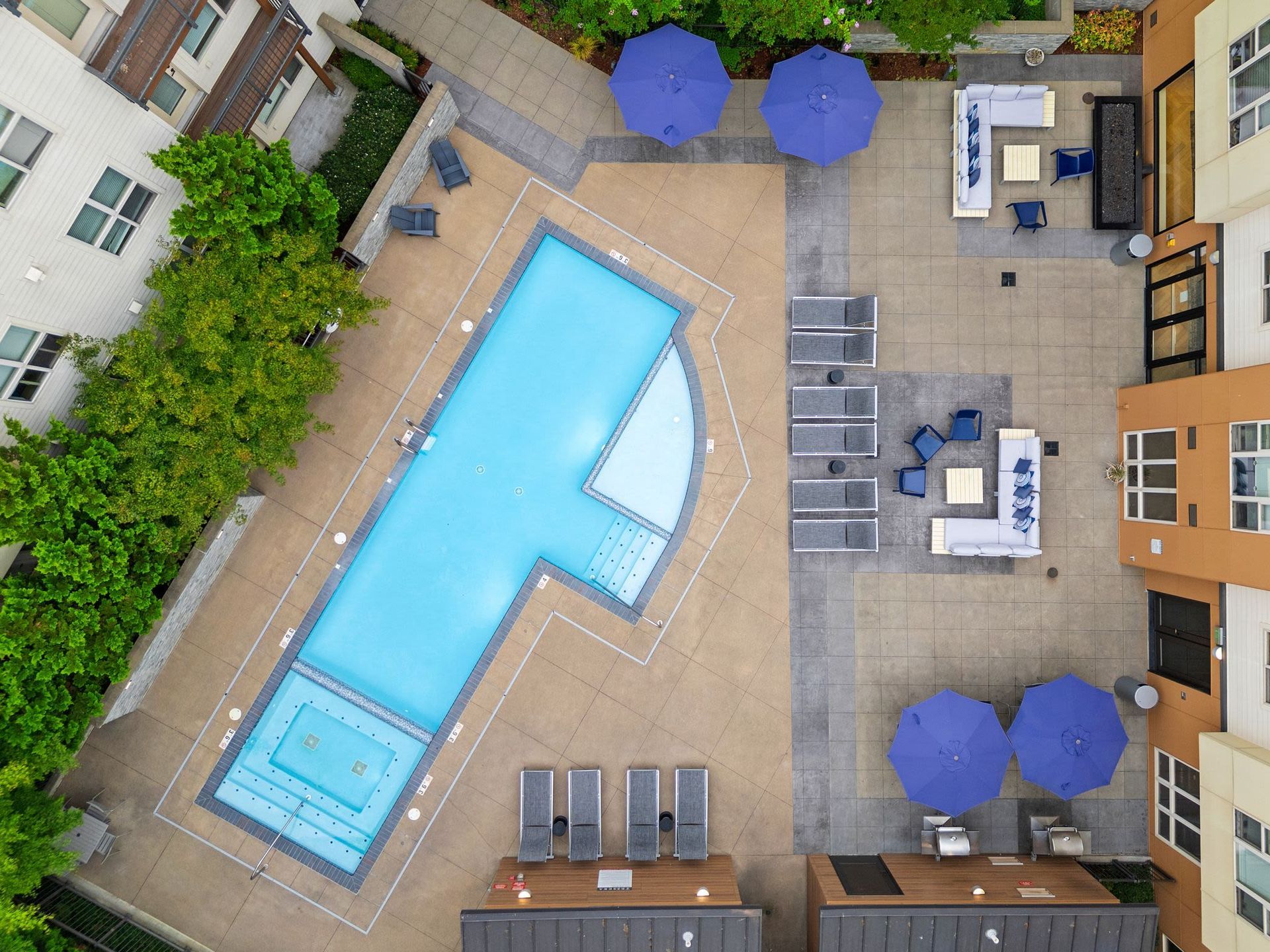 Aerial view of a rectangular pool in an apartment community courtyard with lounge chairs and blue umbrellas at Tessera at Orenco Station.
