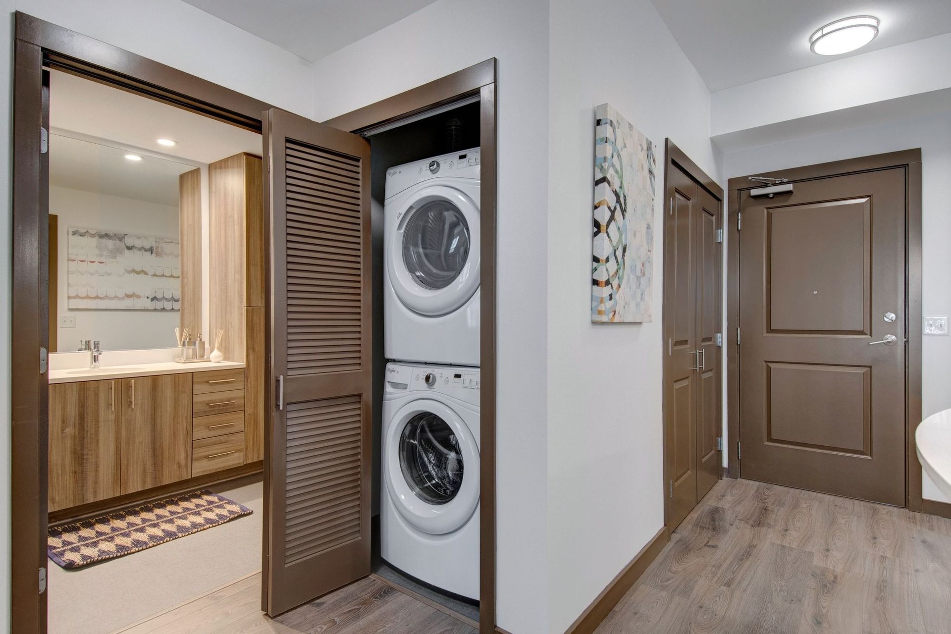 Interior hallway showing stacked washer and dryer in a closet next to a bathroom with wood vanity at Tessera at Orenco Station.