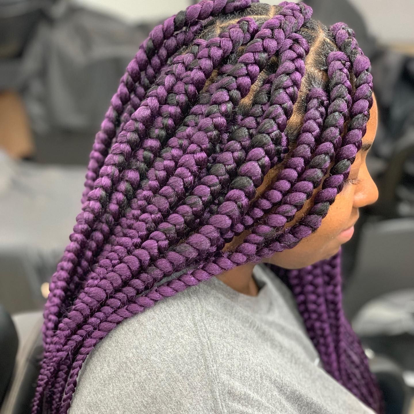 A woman with purple braids is wearing a gray shirt.