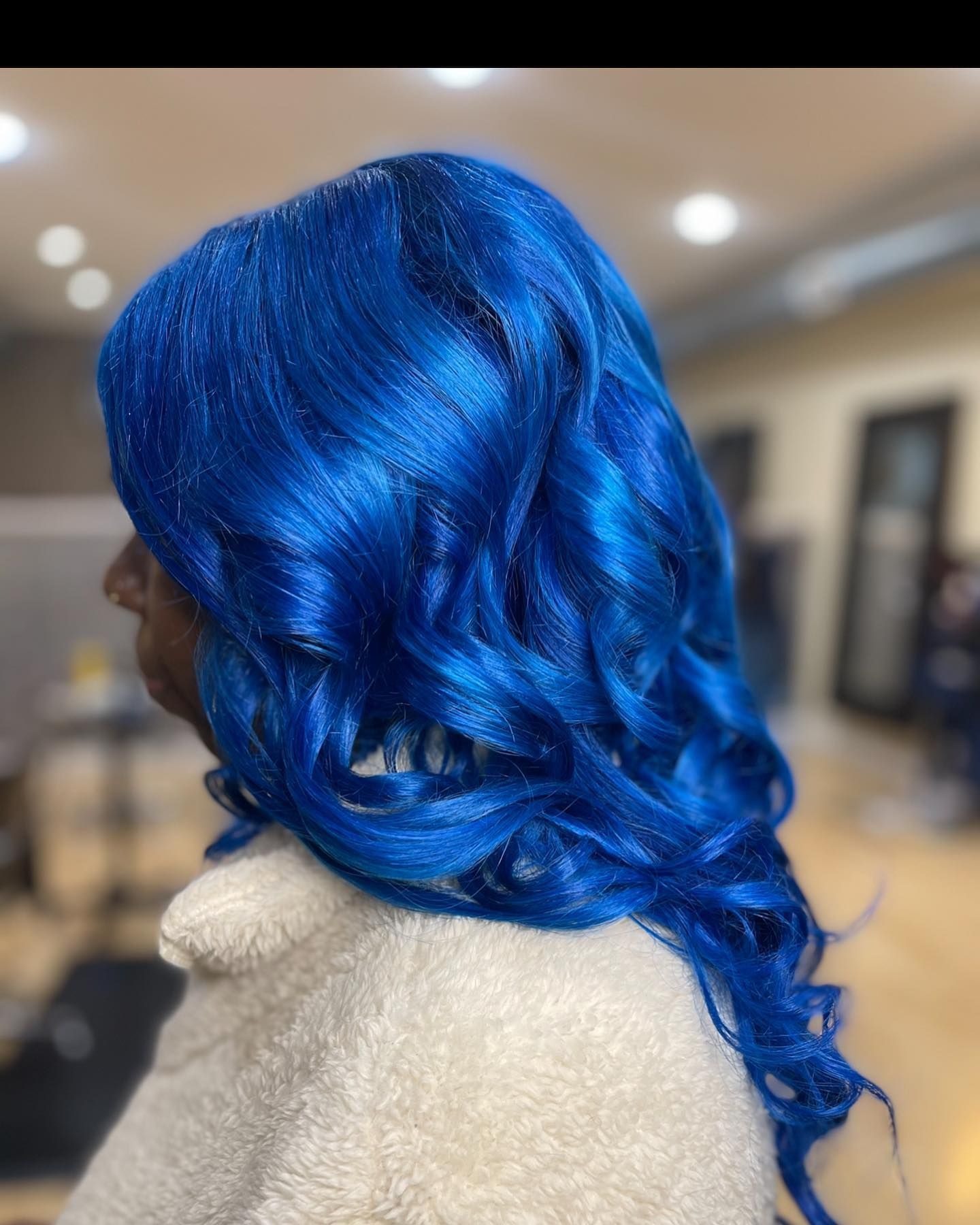 A woman with blue hair is wearing a white coat.
