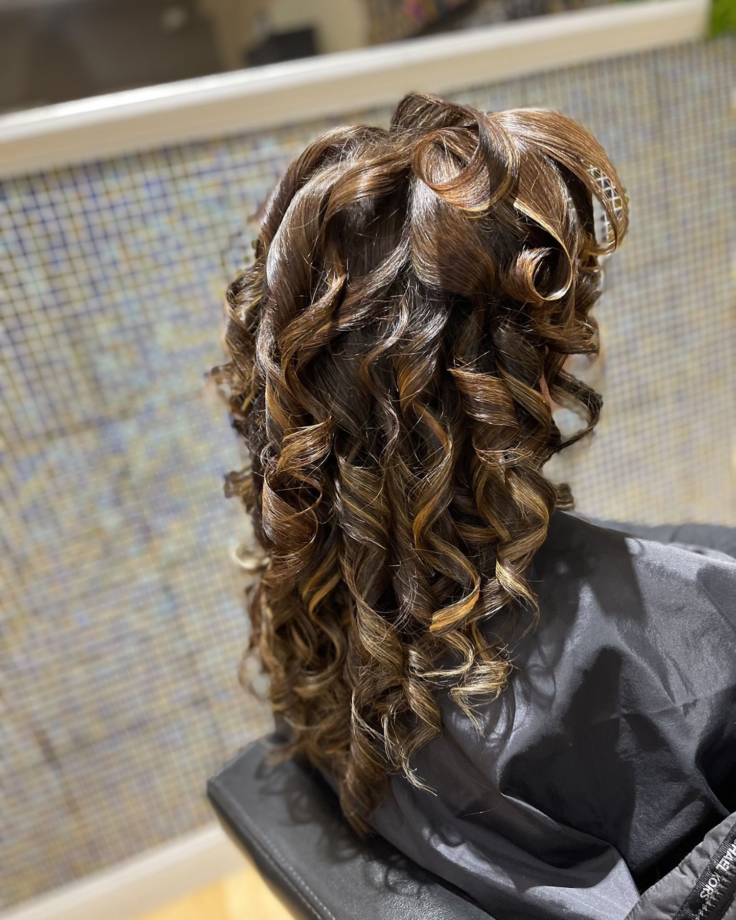 A woman is sitting in a chair with her hair in a half up half down hairstyle.