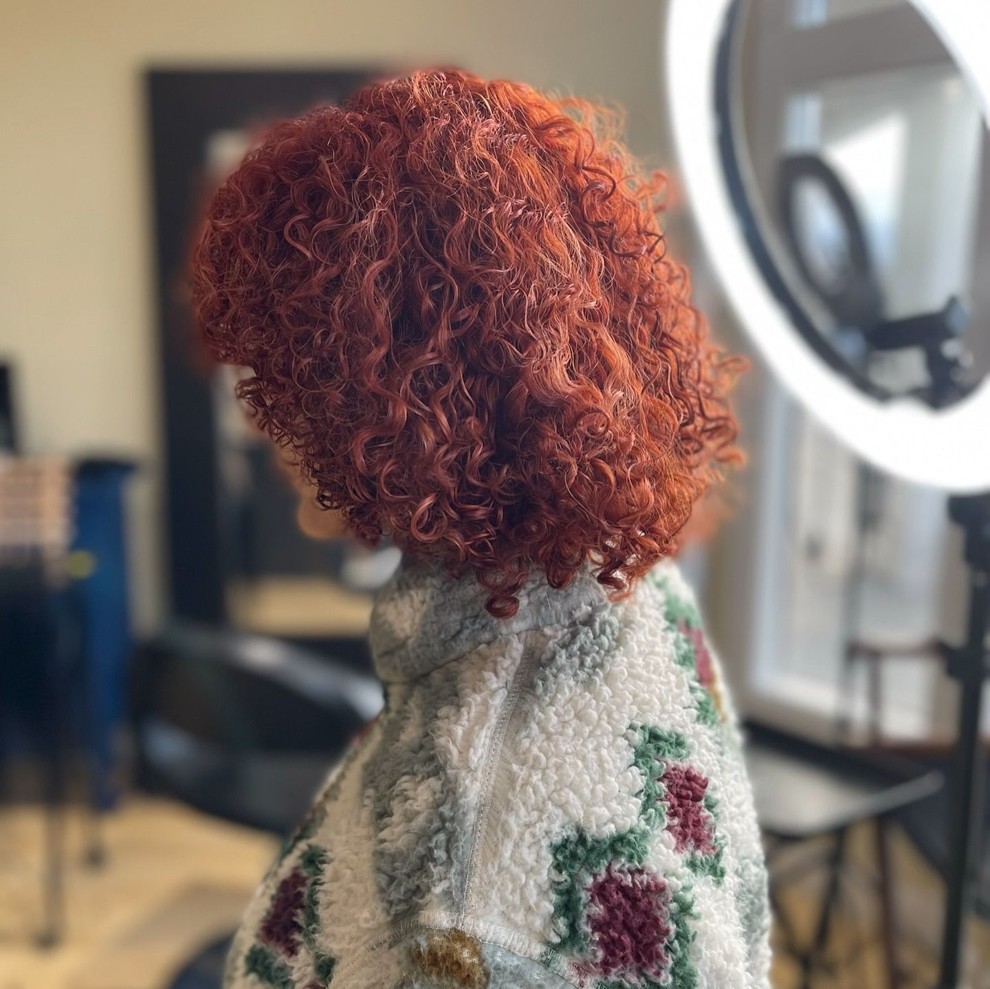A woman with red curly hair is standing in front of a ring light.