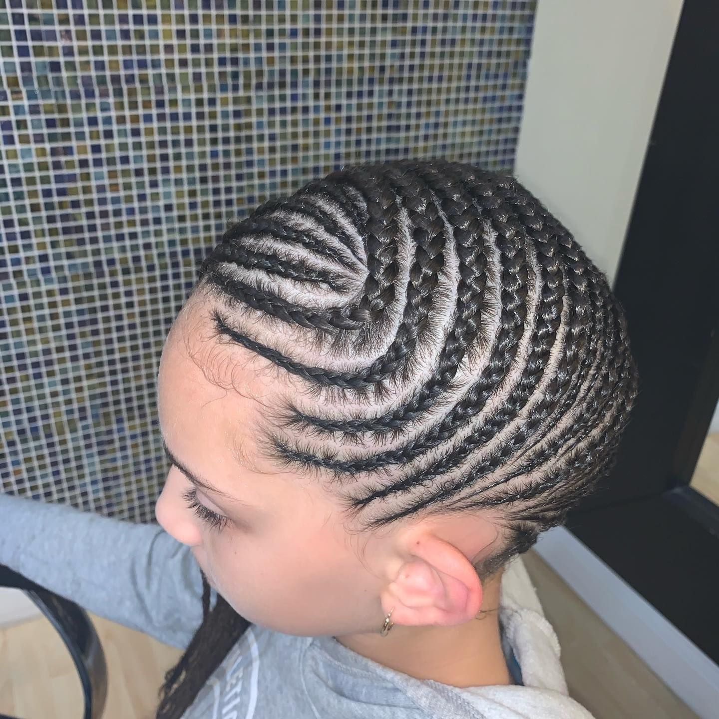 A woman with braids in her hair is standing in front of a tiled wall.