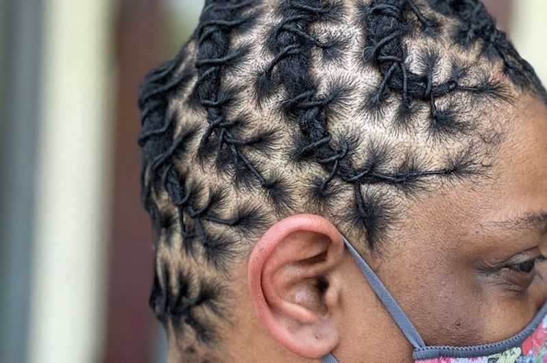 A close up of a person wearing a mask and dreadlocks.