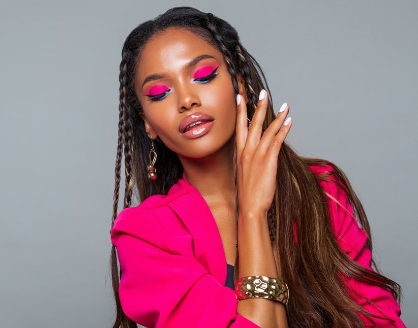 The woman is wearing a pink jacket and earrings and has braids in her hair.