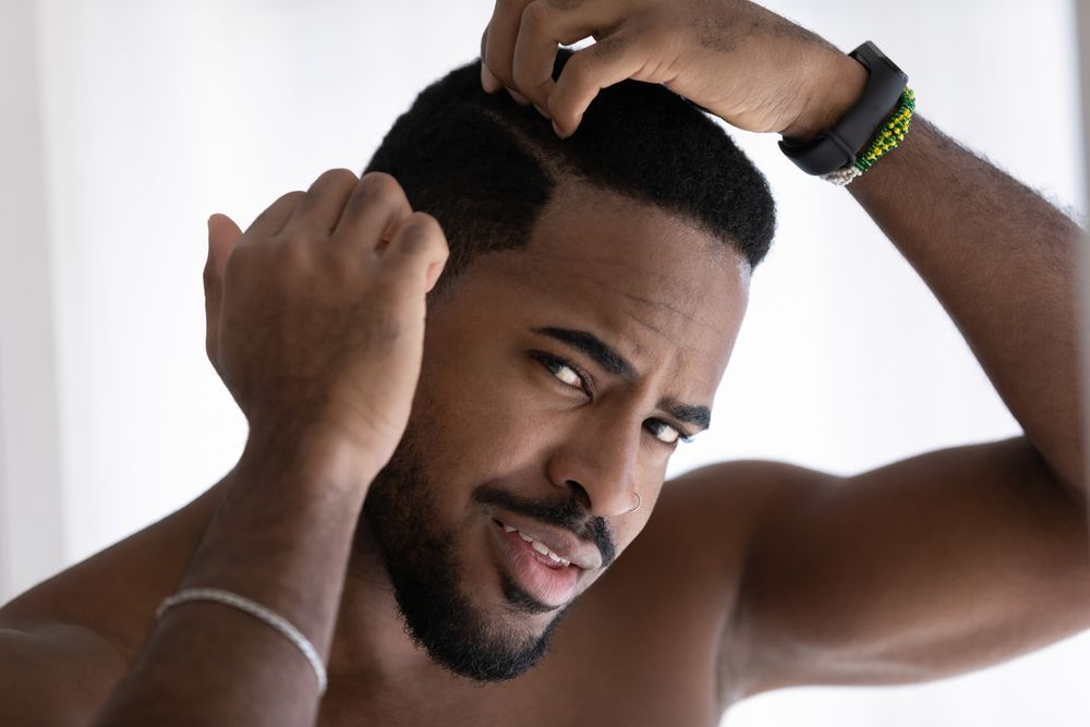 A shirtless man is looking at his hair in the mirror.
