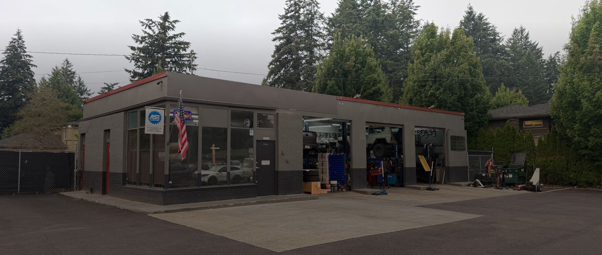 Small roadside fire station with open bays, fire trucks inside, and tall trees in the background | Paul's Automotive