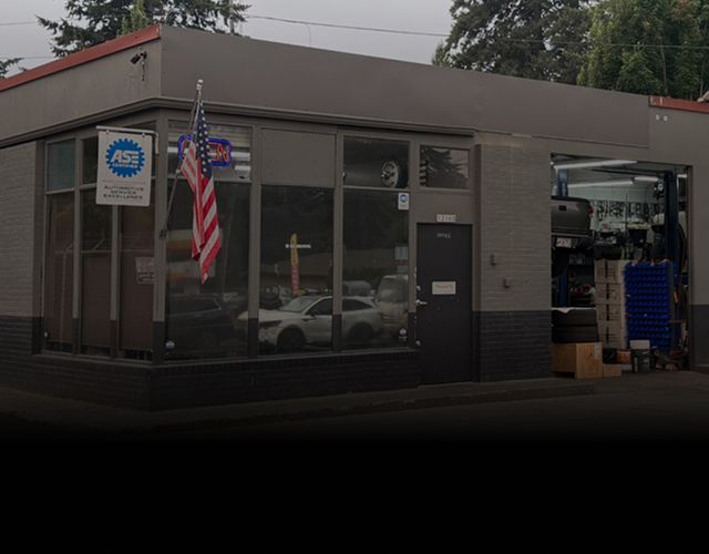 Small storefront with an American flag, glass windows, and a service bay open on the right. | Paul's Automotive