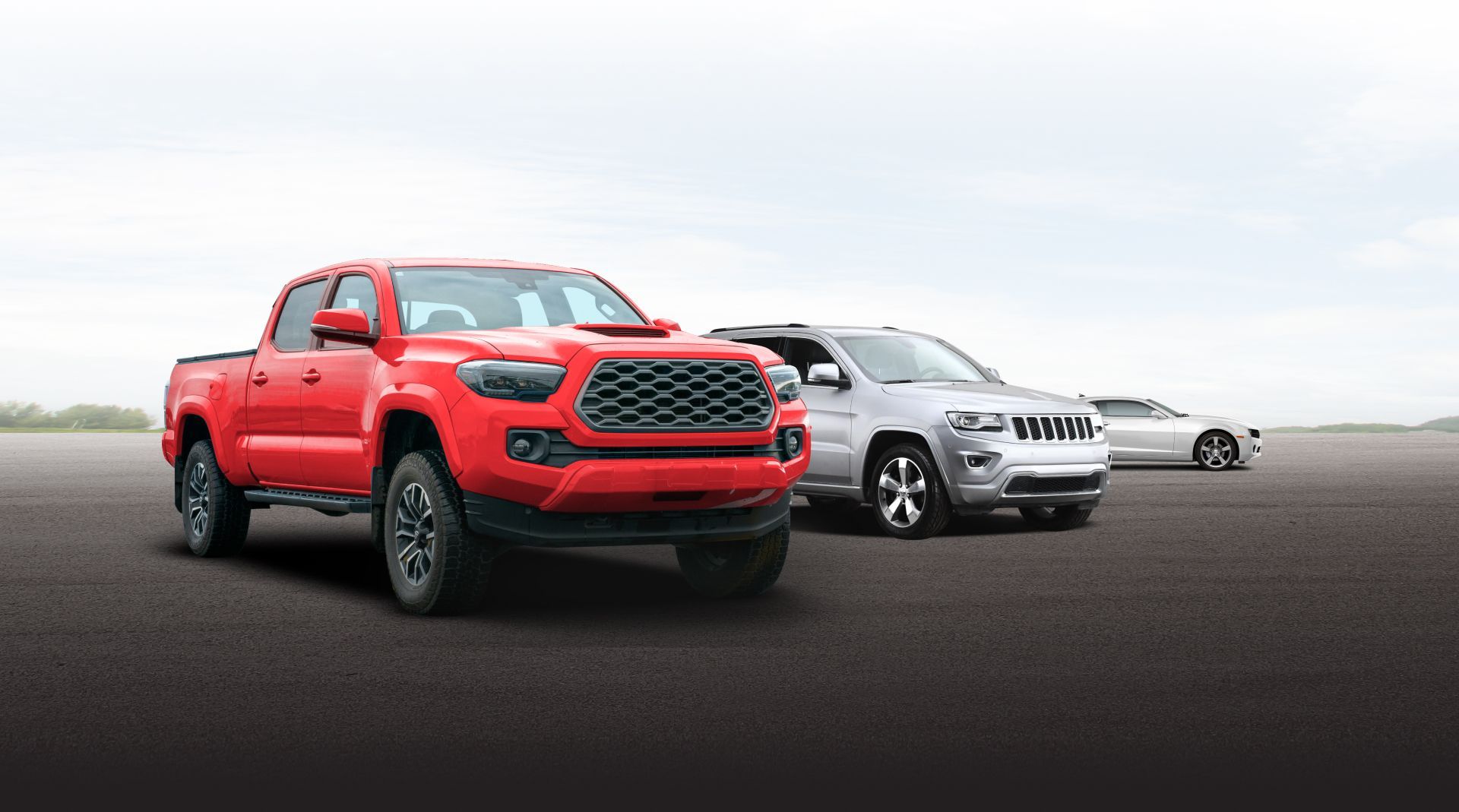 Red pickup truck in front of a silver SUV on a road under a cloudy sky | Paul's Automotive