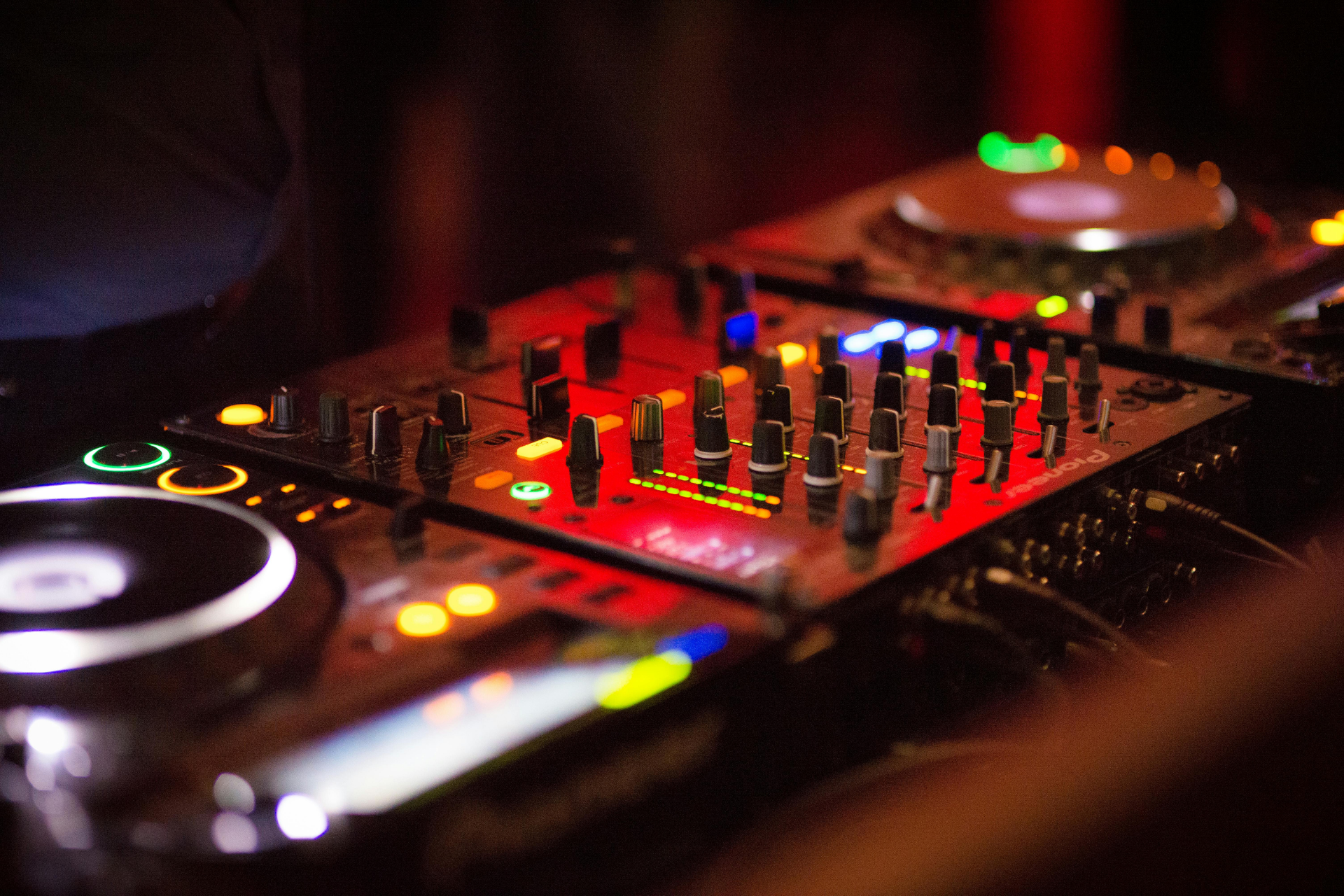 Illuminated DJ mixer with glowing red and green controls in a dark club setting