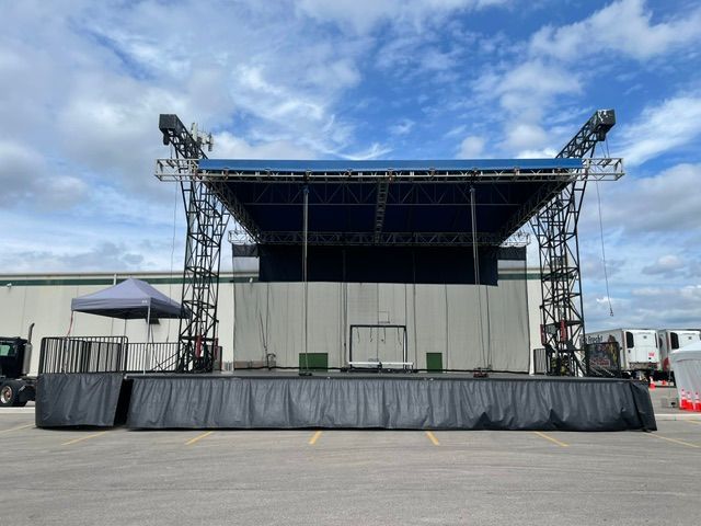 Outdoor concert stage at sunset with lighting rig and equipment cases in front of a large empty screen