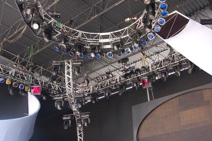 Ceiling rig of stage lights and trusses in an indoor arena, viewed from below