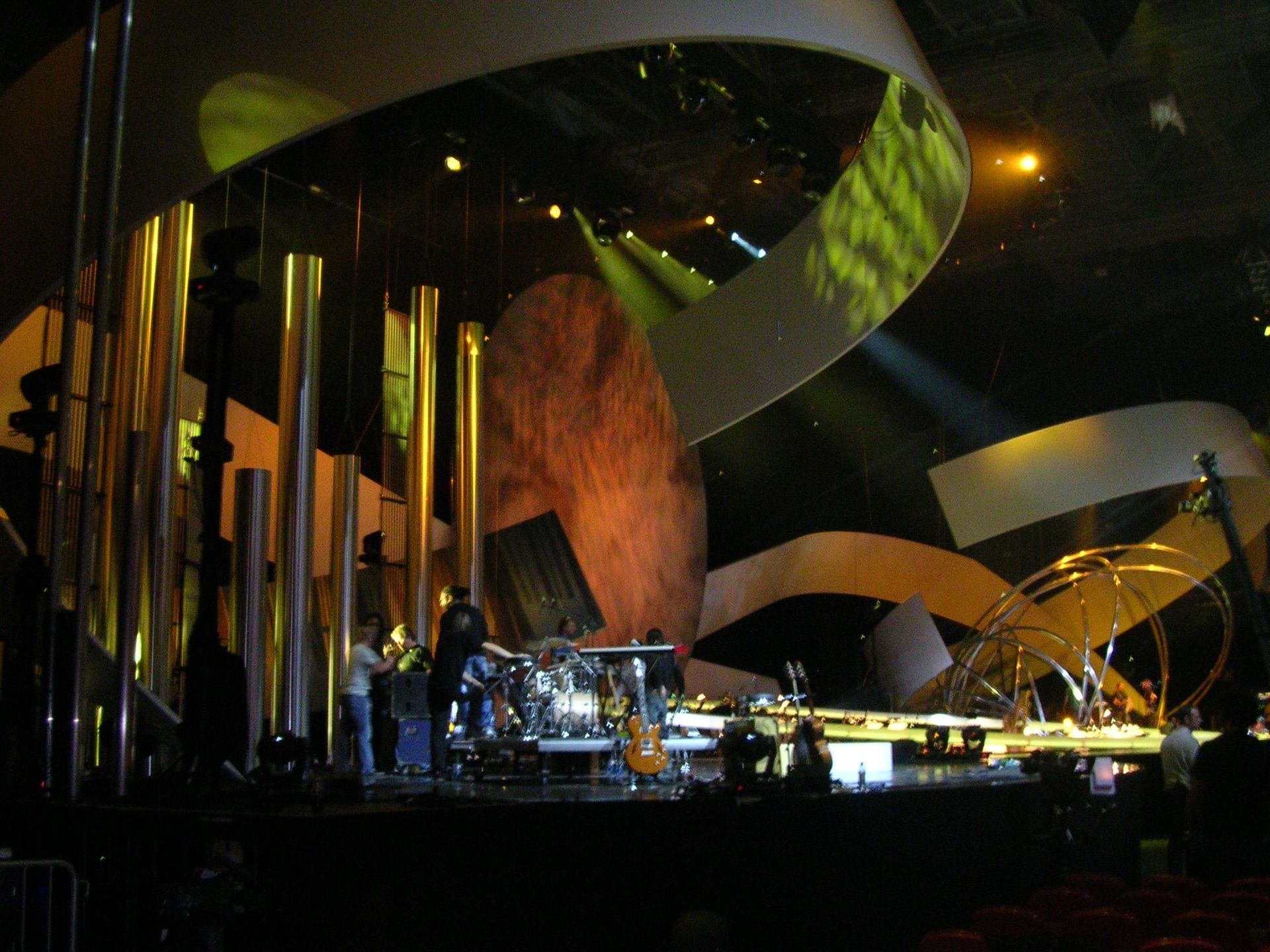Nighttime outdoor concert stage with large curved sculptures and musicians under warm lights