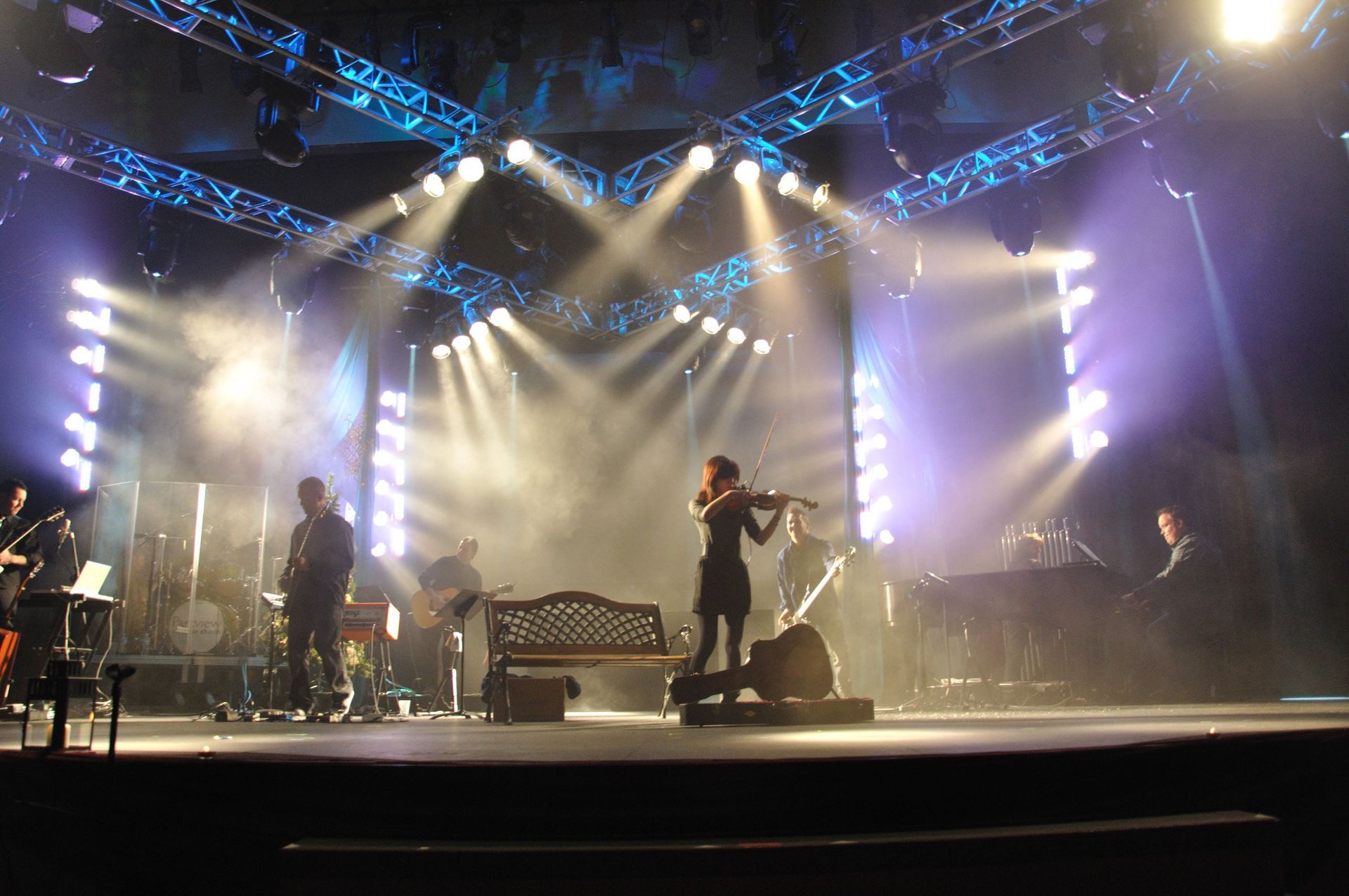 Concert stage with bright spotlights, band silhouettes, and a singer performing center stage