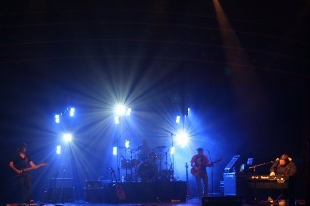 Blue-lit concert stage with band performing under bright spotlights