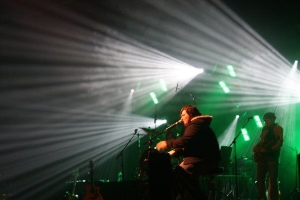 Live concert with musicians on stage under green and white spotlights