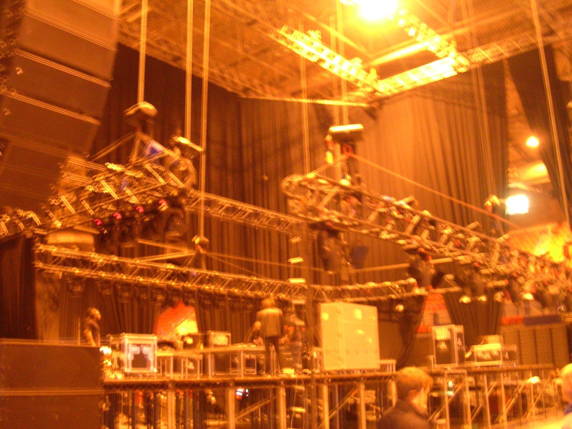 Orange-lit stage with overhead truss lighting and crew equipment in a large indoor venue