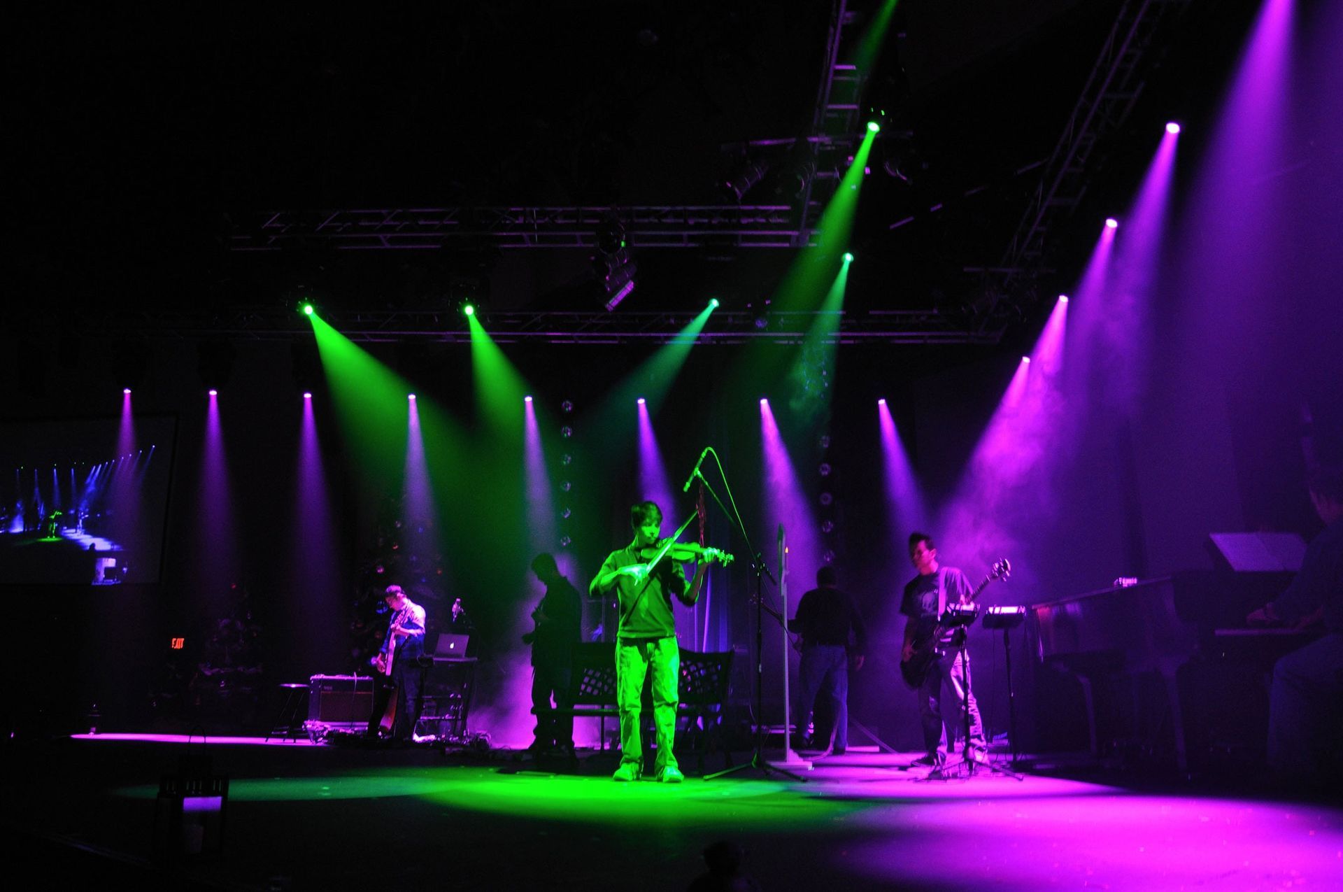 Live band performing on a dark stage under green and purple spotlights