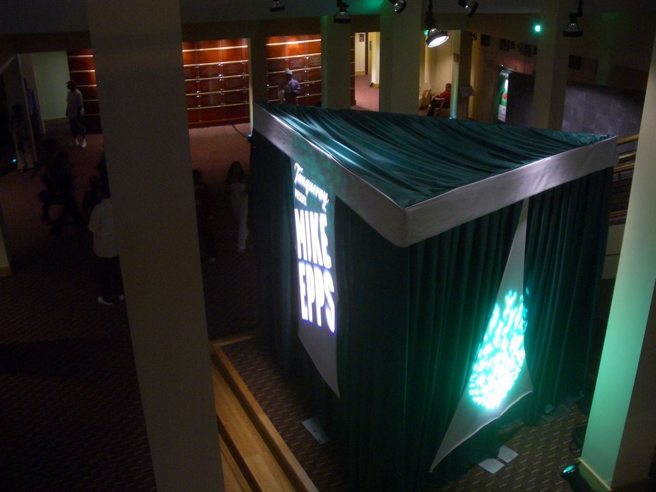 Illuminated black cube art installation in a dim indoor gallery, with glowing green-white graphics on its sides