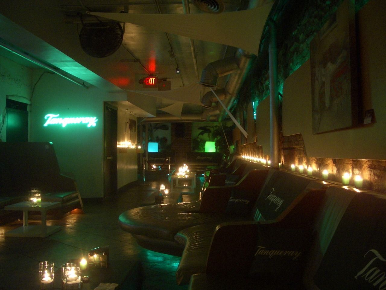 Dim lounge with green neon lights, candles, and empty chairs in a cozy bar-like setting