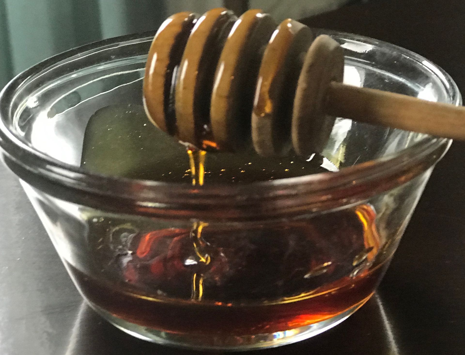 Wooden honey wand dipped into a small glass bowl dripping with honey. 