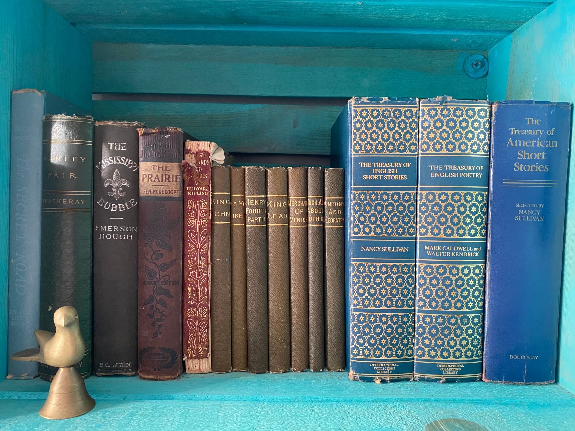 Various old or classic books, large sizes to small set side by side within teal blue carton shelving. 