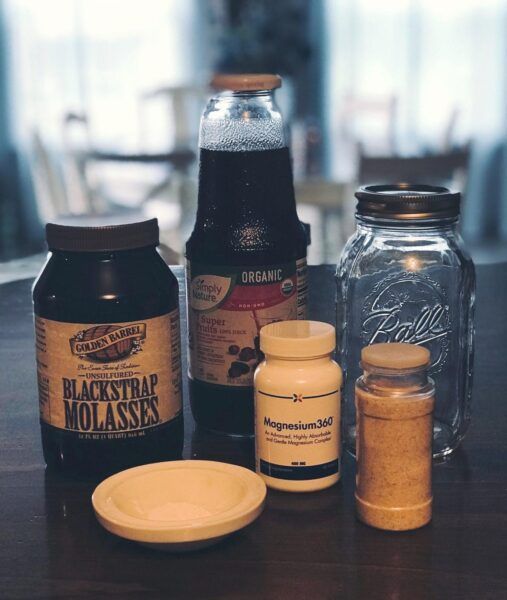 Blackstrap, organic non-concentrated fruit juice, magnesium, mineral salt, canning jar, mortar arranged on wooden counter.