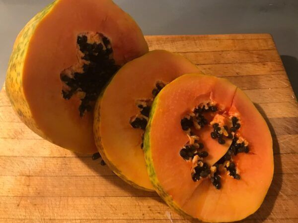 Three thick slices of (orange) papaya containing round black seeds in the center, laid on wooden cutting board.