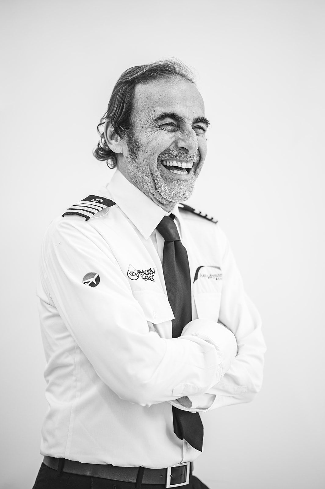 Piloto de avión sonriente, con uniforme blanco y los brazos cruzados, sobre un fondo liso