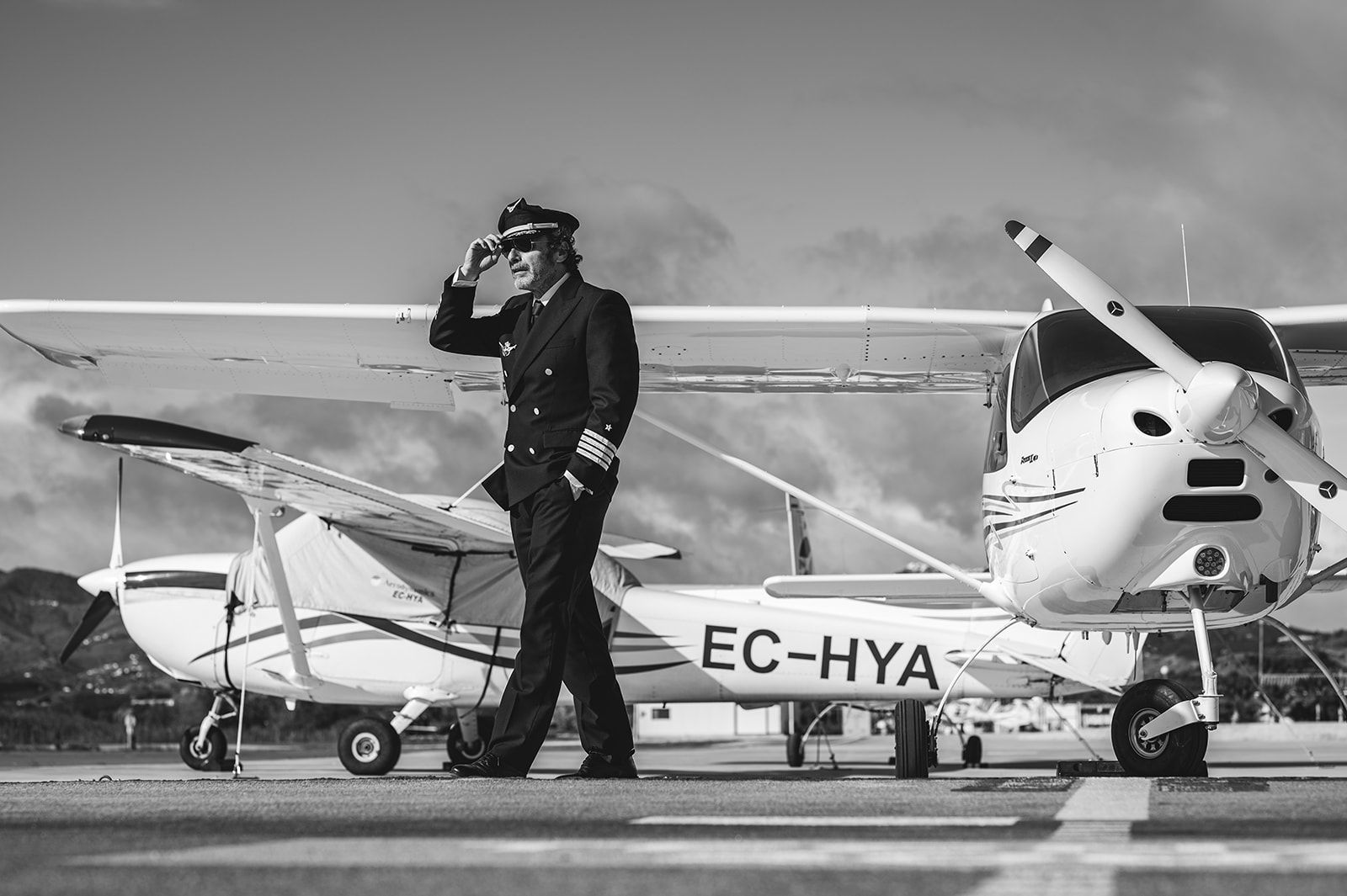 Piloto junto a una avioneta en la pista, escena en blanco y negro, matrícula EC-HYA visible