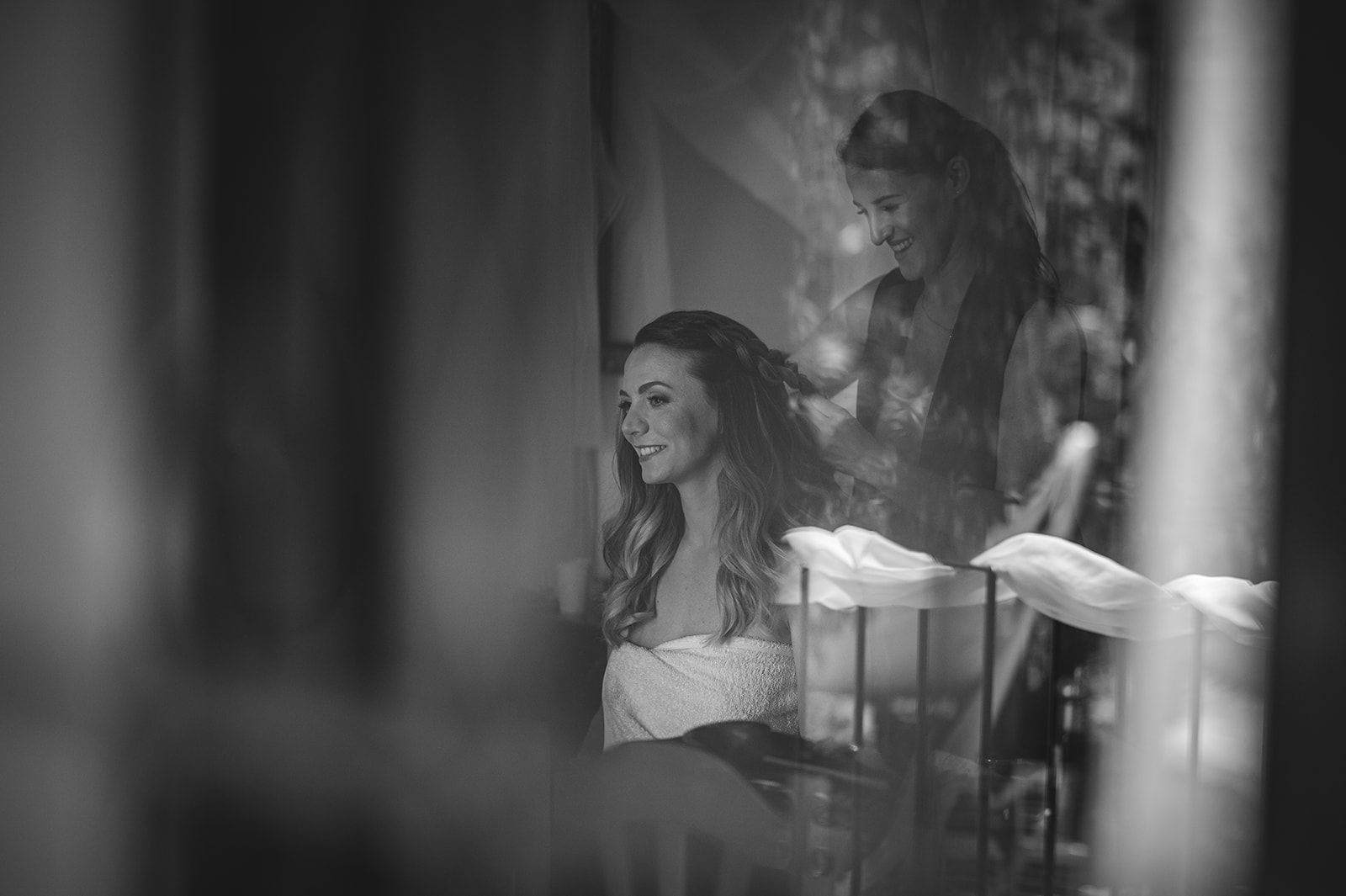La novia sonríe en una foto de boda en blanco y negro, sentada cerca de un hombre al fondo.