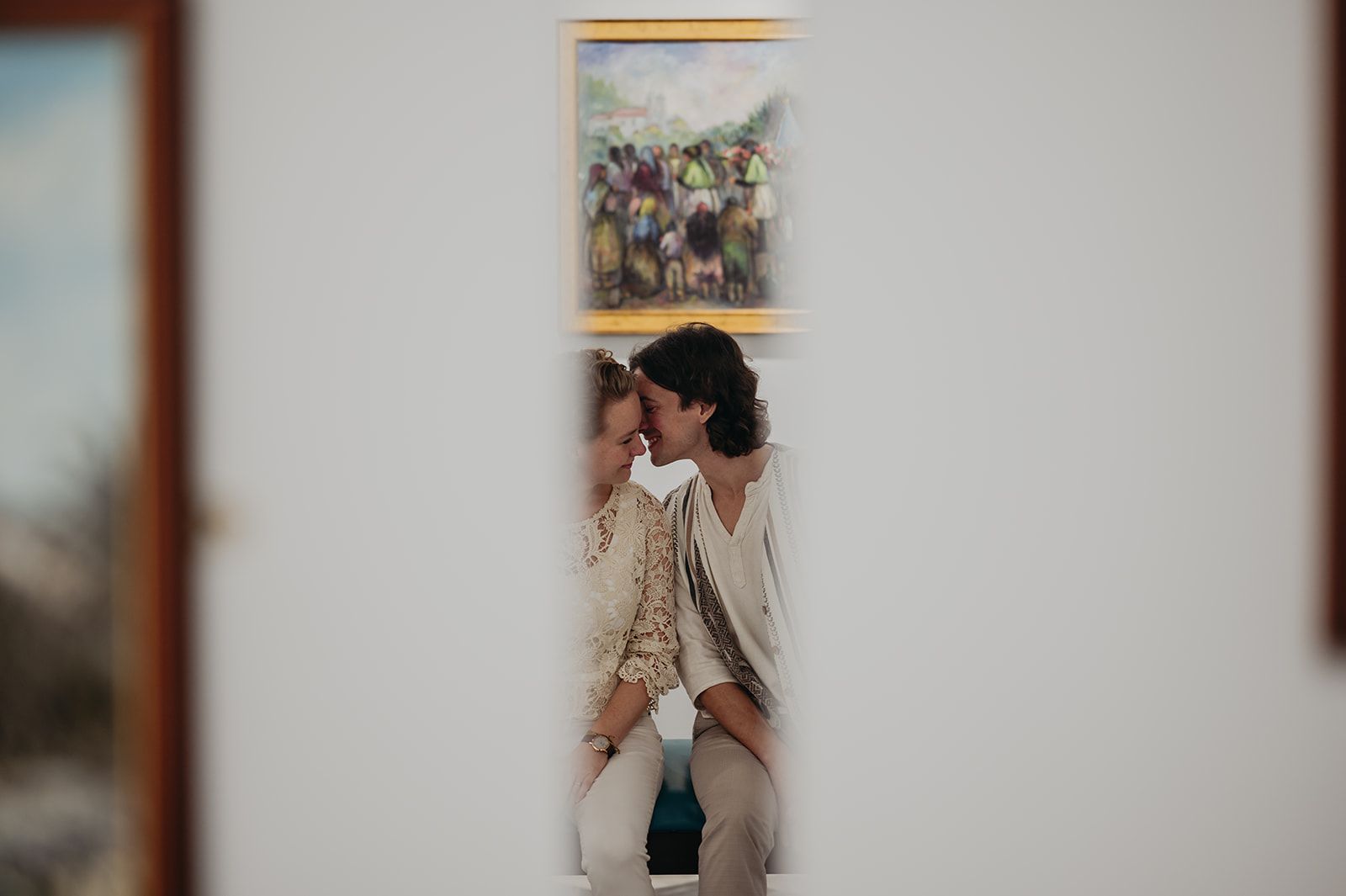 Una pareja besándose en una cama, enmarcada por una puerta en una habitación con luz tenue.