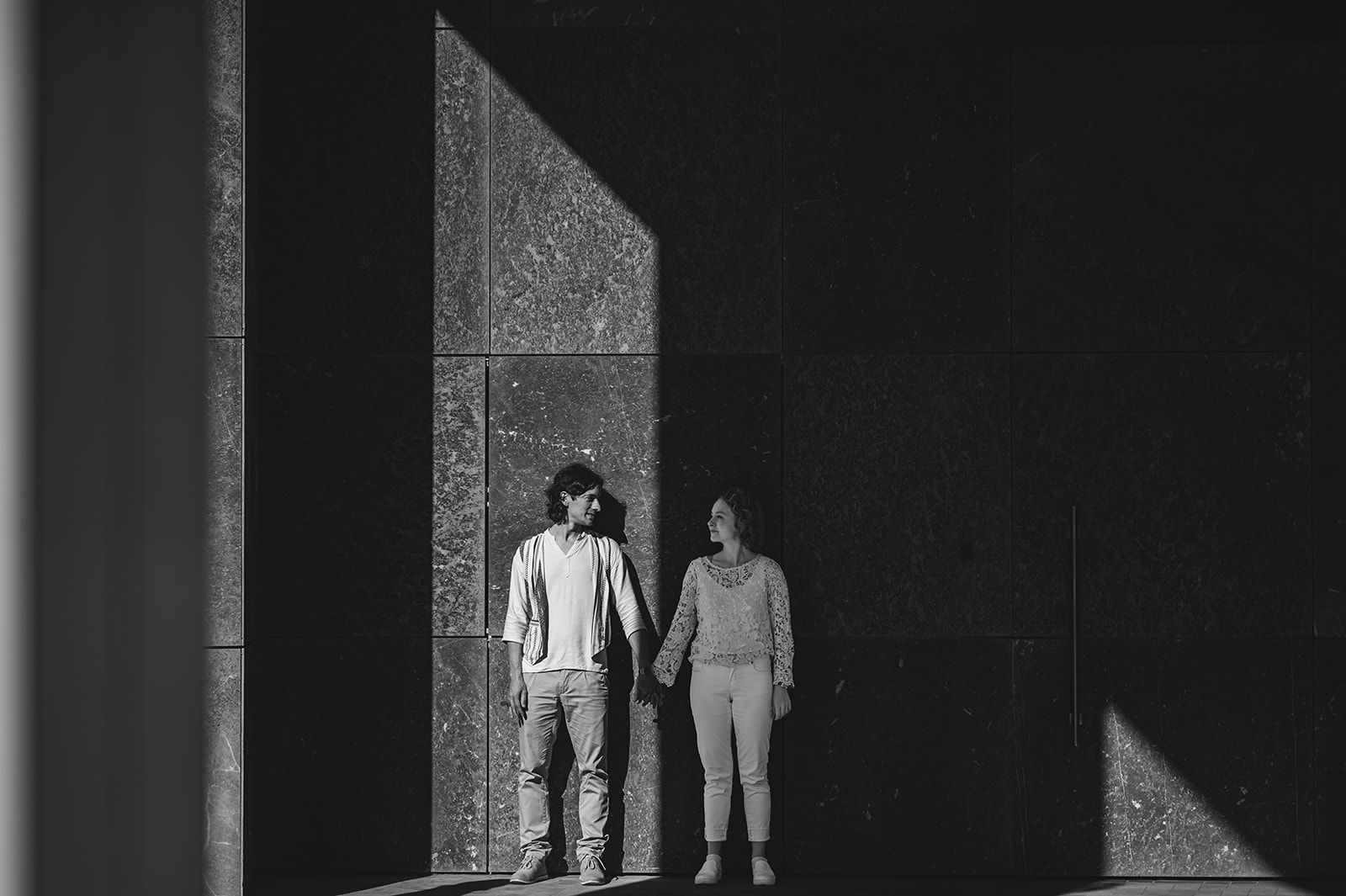Dos personas de pie en un espacio oscuro de formas geométricas, iluminado por el escenario con marcados contrastes de luz y sombra