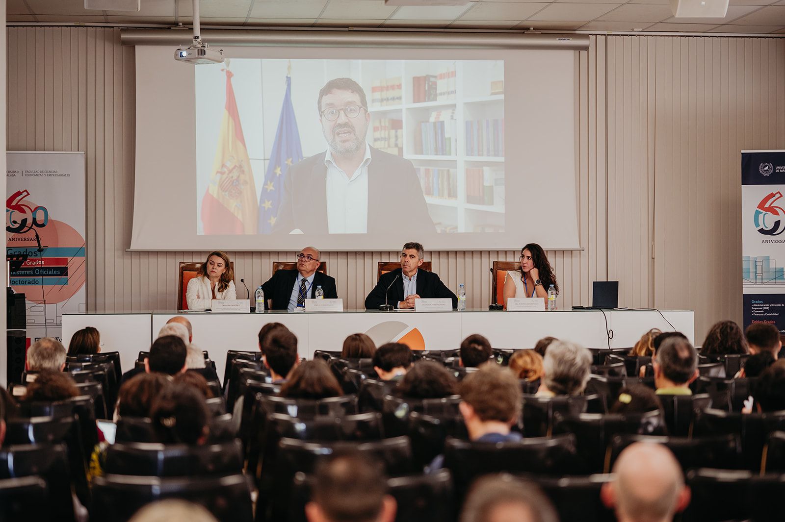 Debate en una sala de conferencias con cuatro ponentes y una videollamada proyectada en una pantalla grande