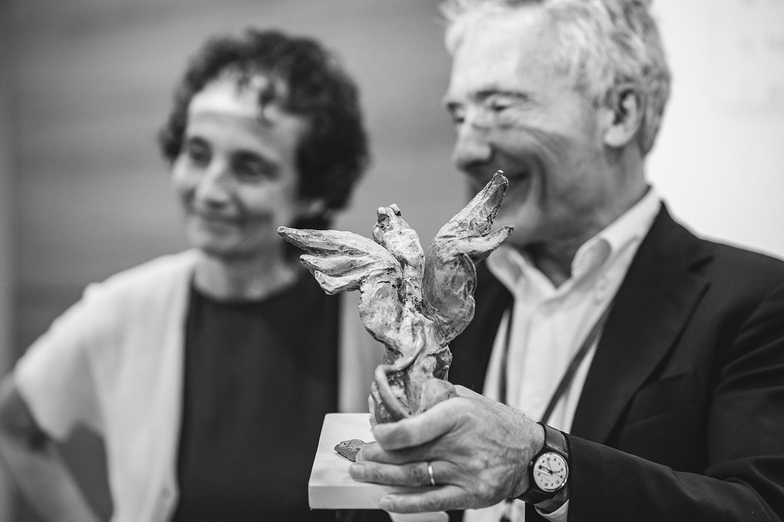 Dos personas sonrientes, una de ellas sostiene un trofeo con forma de pájaro en una foto en blanco y negro de una ceremonia de premios