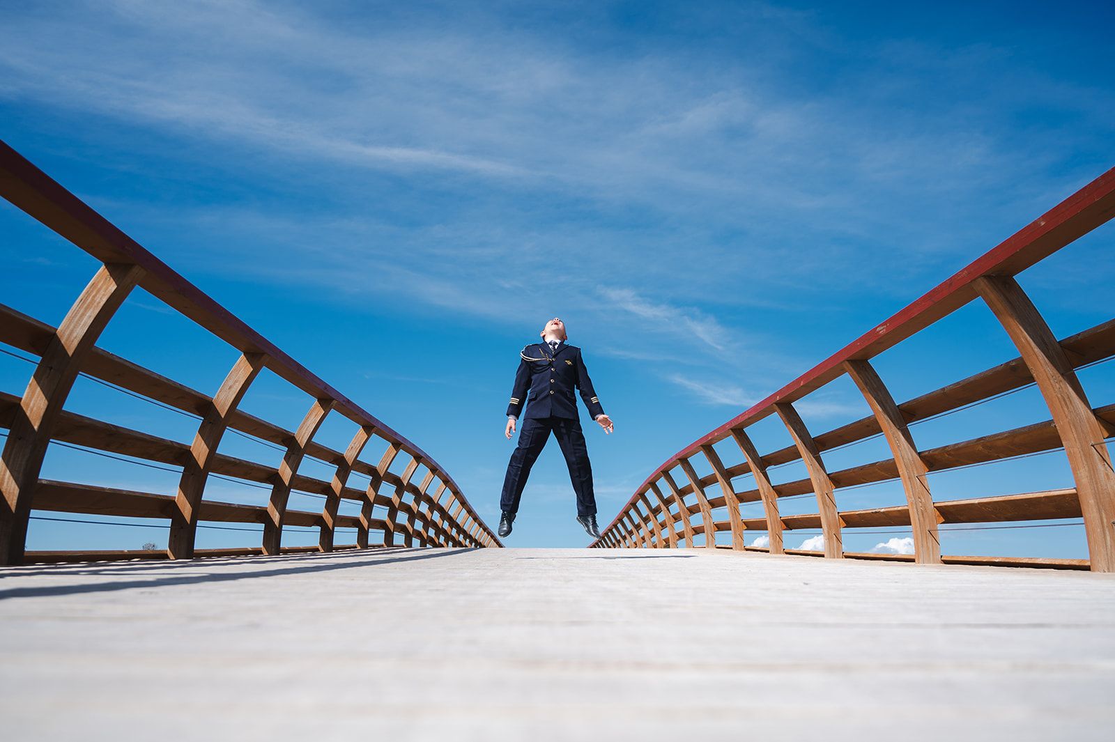 Una persona de pie en un puente de madera bajo un cielo azul, con barandillas de color óxido que convergen en perspectiva