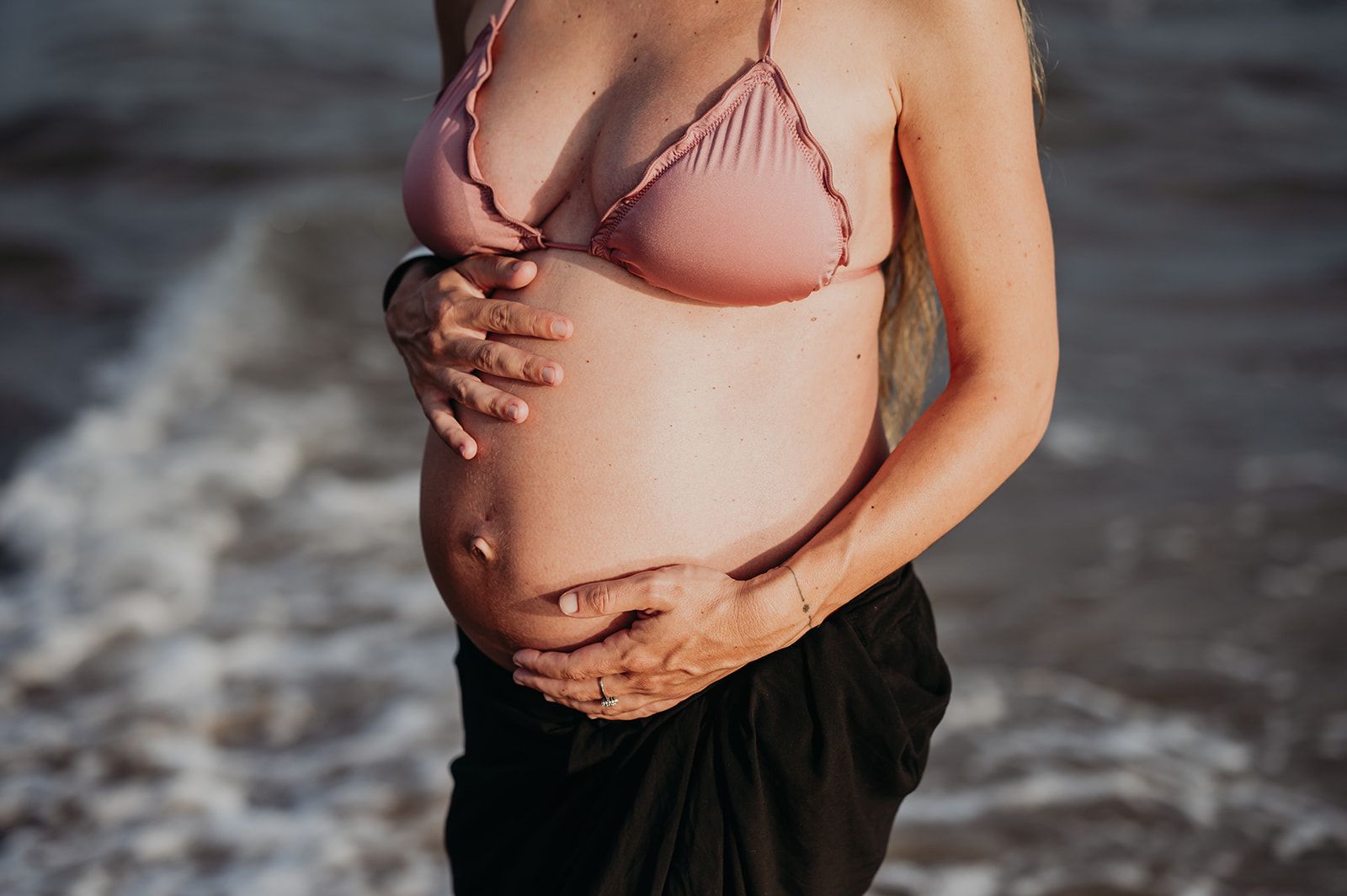 Persona embarazada con un bikini rosa de pie en aguas poco profundas en la playa