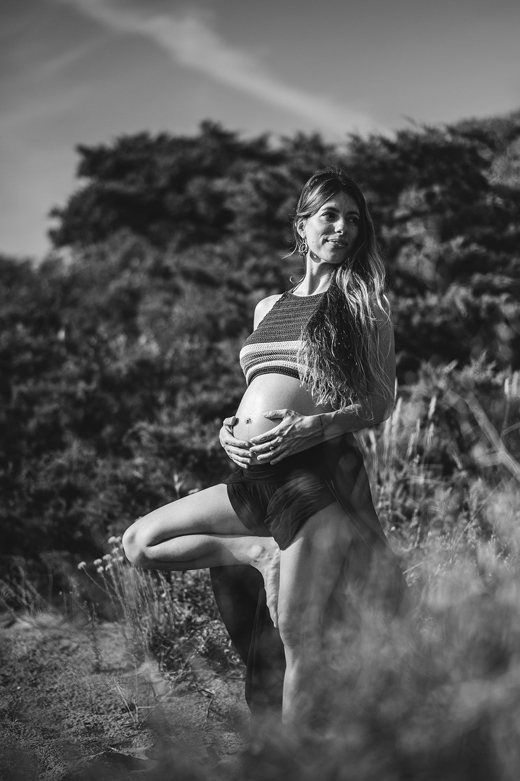 Una mujer de pie entre la hierba alta, sosteniendo una cesta, con árboles al fondo.