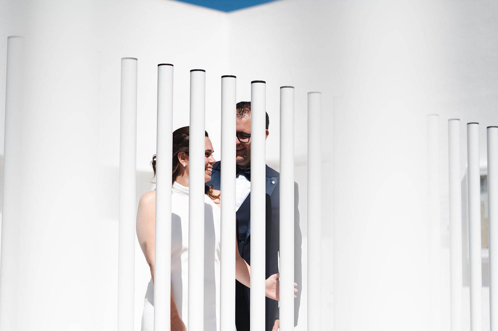 Personas de pie detrás de listones verticales blancos en una habitación muy luminosa y blanca