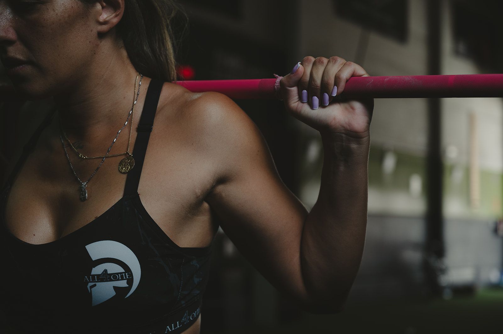Mujer sujetando una barra roja en un gimnasio, con un top deportivo negro.