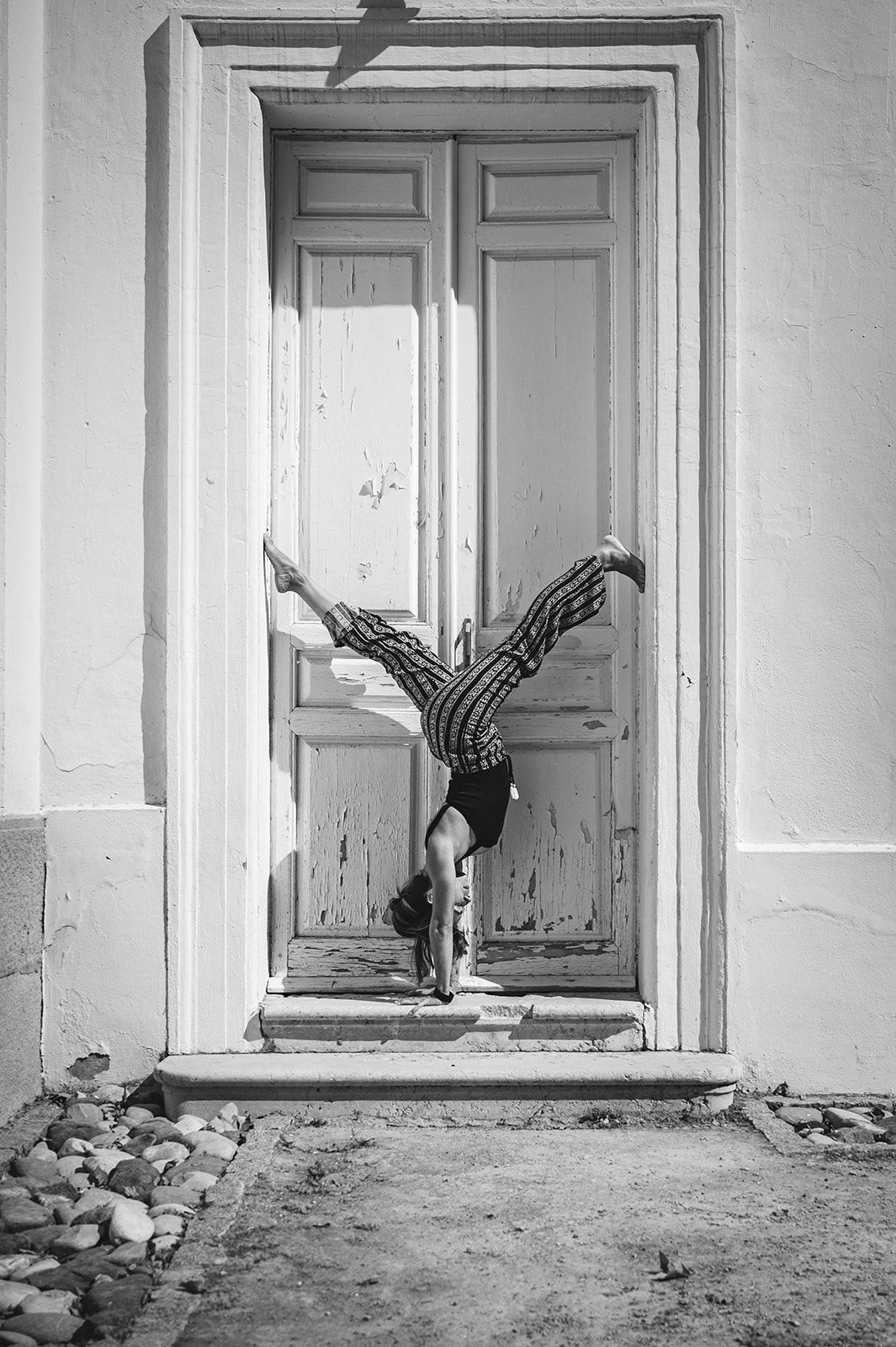 Persona haciendo el pino en el umbral de un edificio deteriorado, con las piernas bien abiertas.