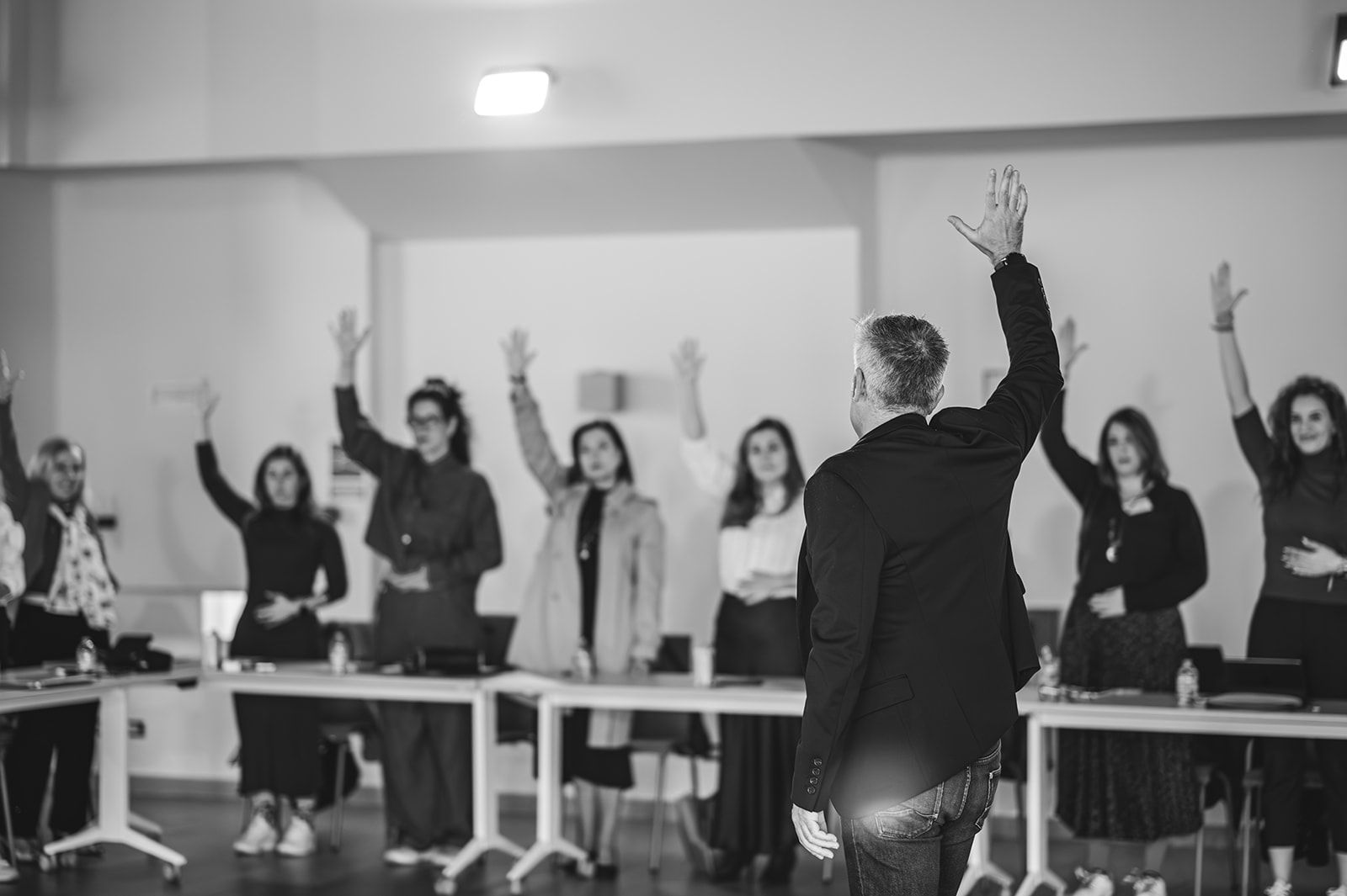 Grupo de personas en una sala levantando la mano durante una reunión o clase