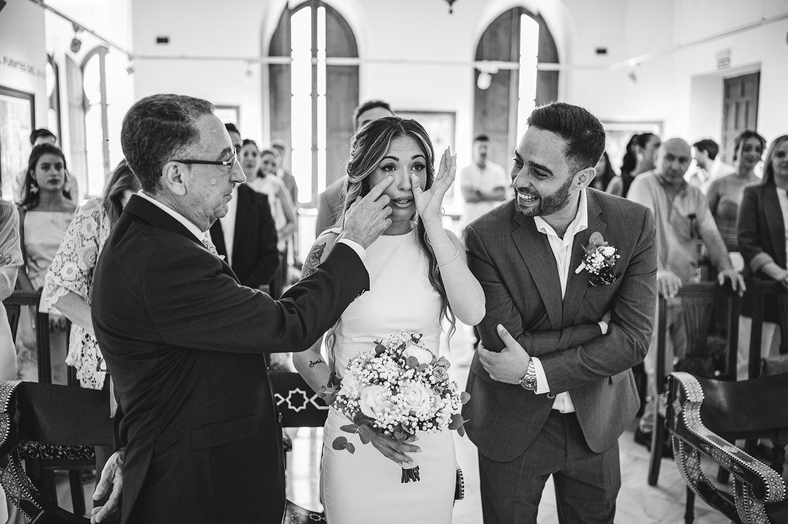 Ceremonia de boda con los novios sonrientes mientras el oficiante le acomoda el velo a la novia dentro de una iglesia