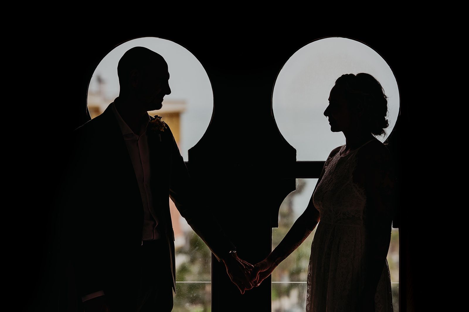 Pareja en silueta cogida de la mano frente a unas ventanas circulares luminosas