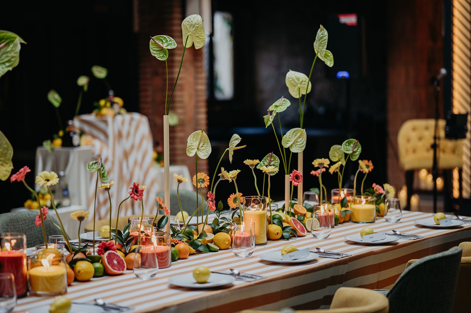 Larga mesa de banquete con fruta, velas y centros de mesa florales en un comedor cálidamente iluminado